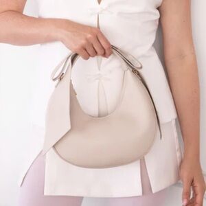 Cream AOTA Brand Circle Purse with Bow and Gold Colored Metal Hardware Crossbody